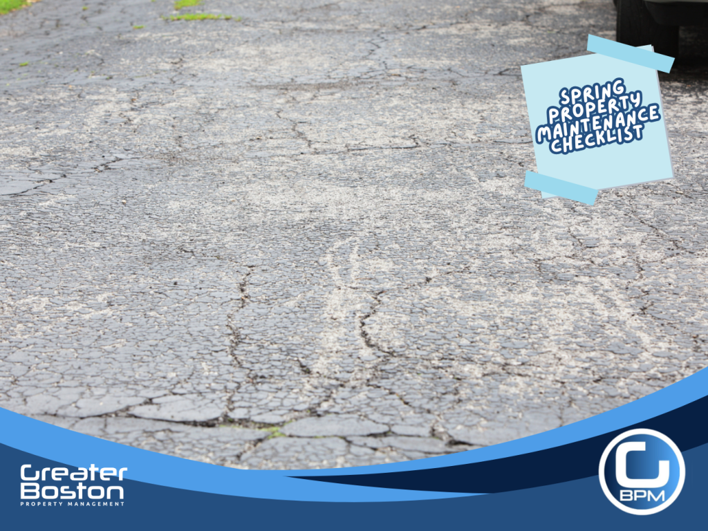 Cracked driveway surface showing damage from winter freeze thaw cycles requiring repair during spring property maintenance.