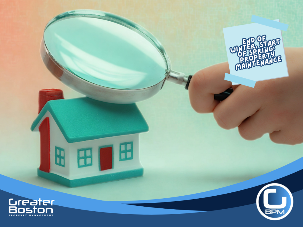 Hand holding magnifying glass inspecting small house model for winter damage before spring property maintenance.