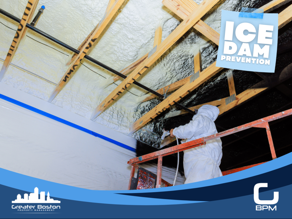 Contractor in protective suit spraying closed-cell foam insulation on attic roof rafters of Boston condo building representing the highest-value ice dam prevention intervention of attic air sealing and insulation that stops heat loss before meltwater forms at the eave in 2026